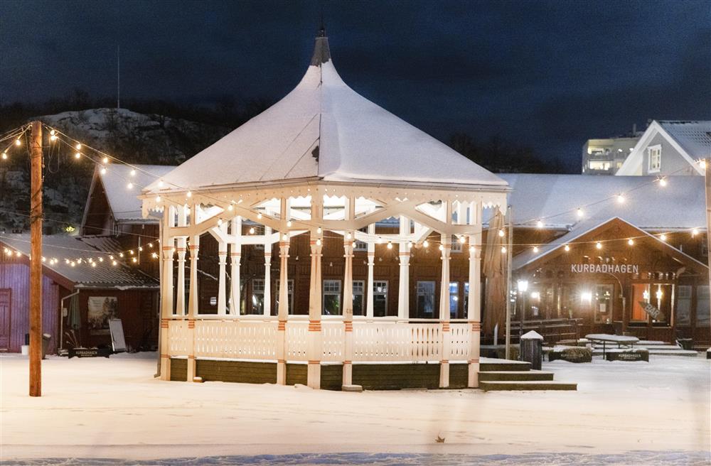 Vinter, lyssatt hvitmalt paviljong med gjerde, foran historisk kurbadbyggninger i dragestil - Klikk for stort bilde