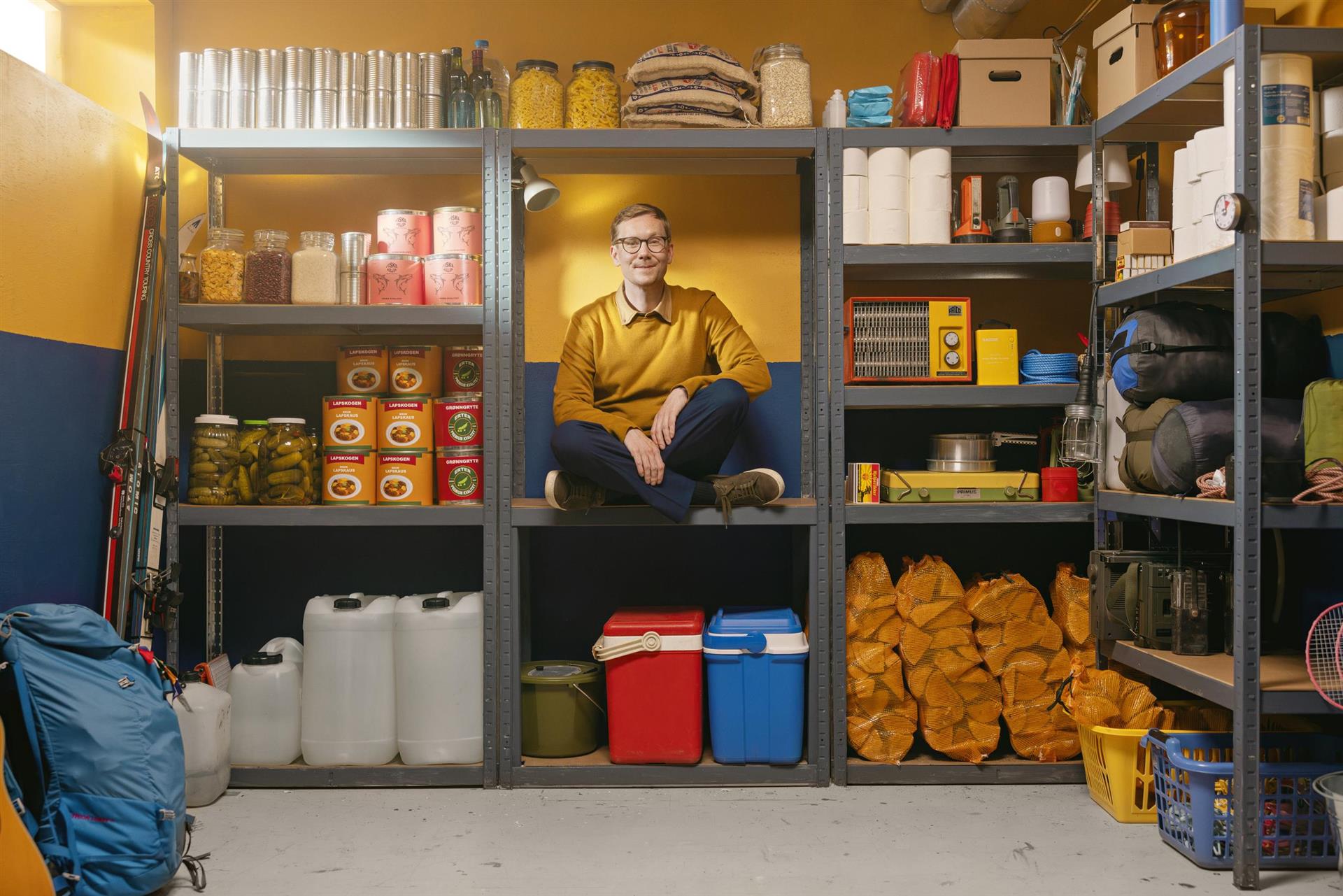 Mann som sitter i en hylle. Rundt seg har han ting som hører til et beredskapslager.