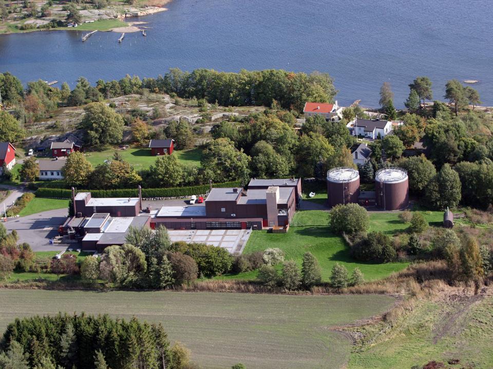 Dronefoto av et bygg som ligger mellom et jorde og sjøen. - Klikk for stort bilde