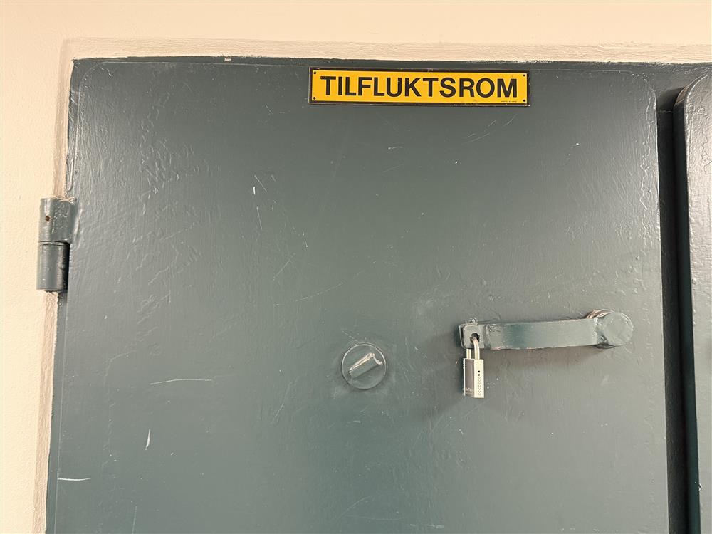Dør med skilt der det står «tilfluktsrom». - Klikk for stort bilde